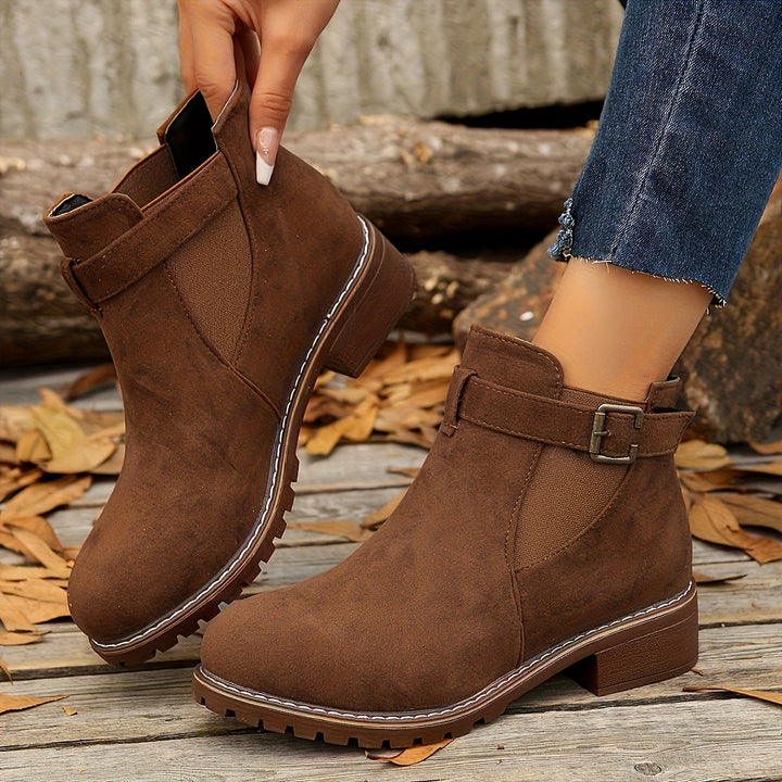 Marigold buckle strap Chelsea boots held by hand, side view in brown
